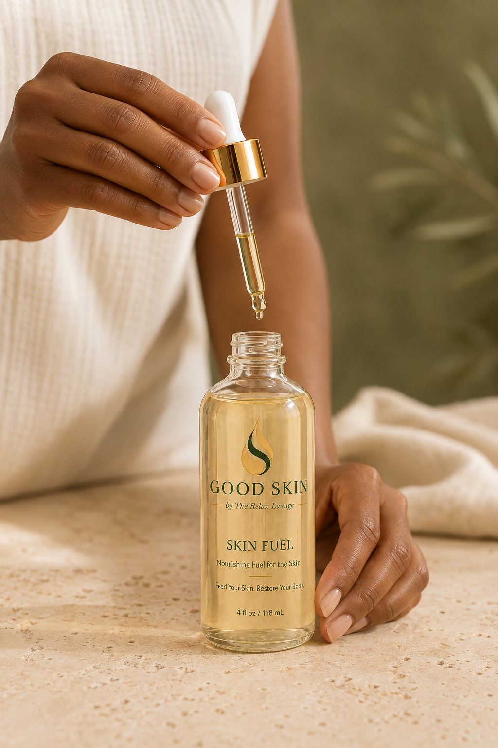 Woman lifting the white and gold dropper from a clear Good Skin Skin Fuel body and massage oil bottle.